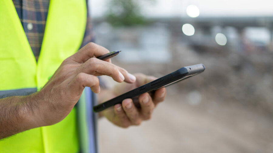 A construction worker using the Estimator360 mobile app on a job site to manage projects